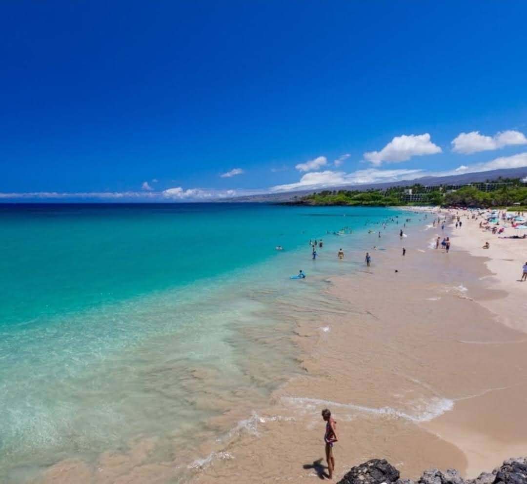Deep blue sky with small clouds over a turquoise bay and a long sandy beach