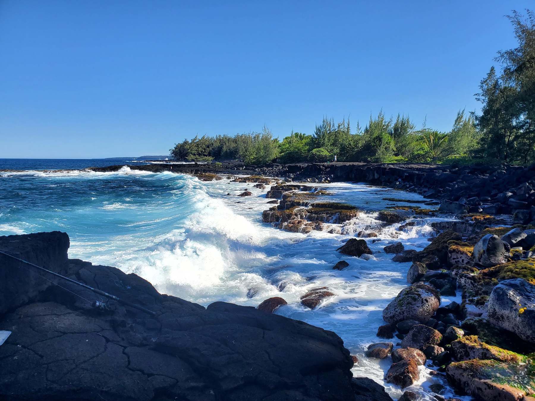 White surf crashing over black lava rock under a deep blue sky