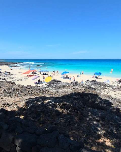 Black lava rock above a busy turquoise beach